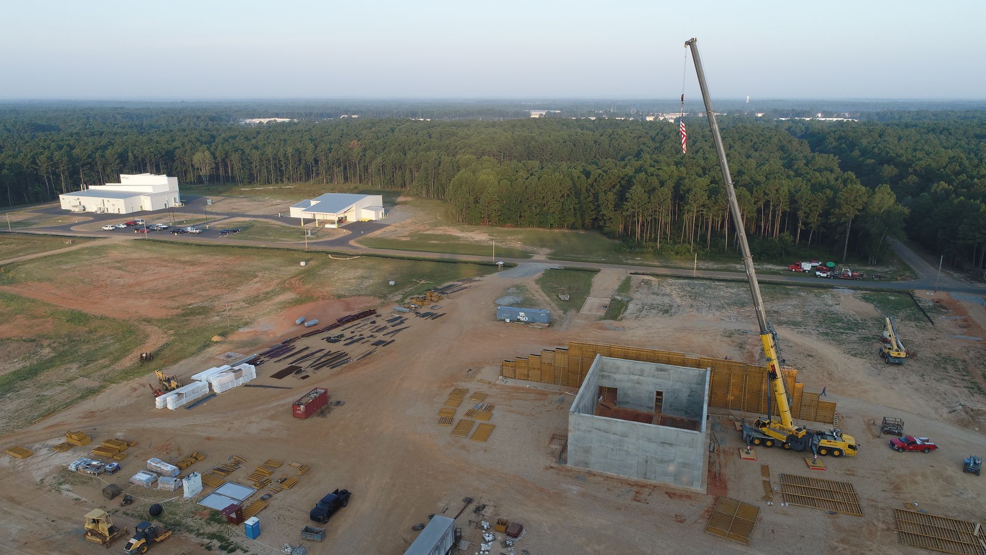 Construction site with crane, concrete foundation, equipment, and forest in the background