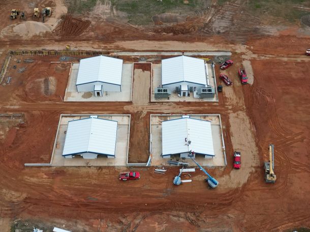 Aerial view of four white tents on a cleared red dirt site with construction vehicles nearby.