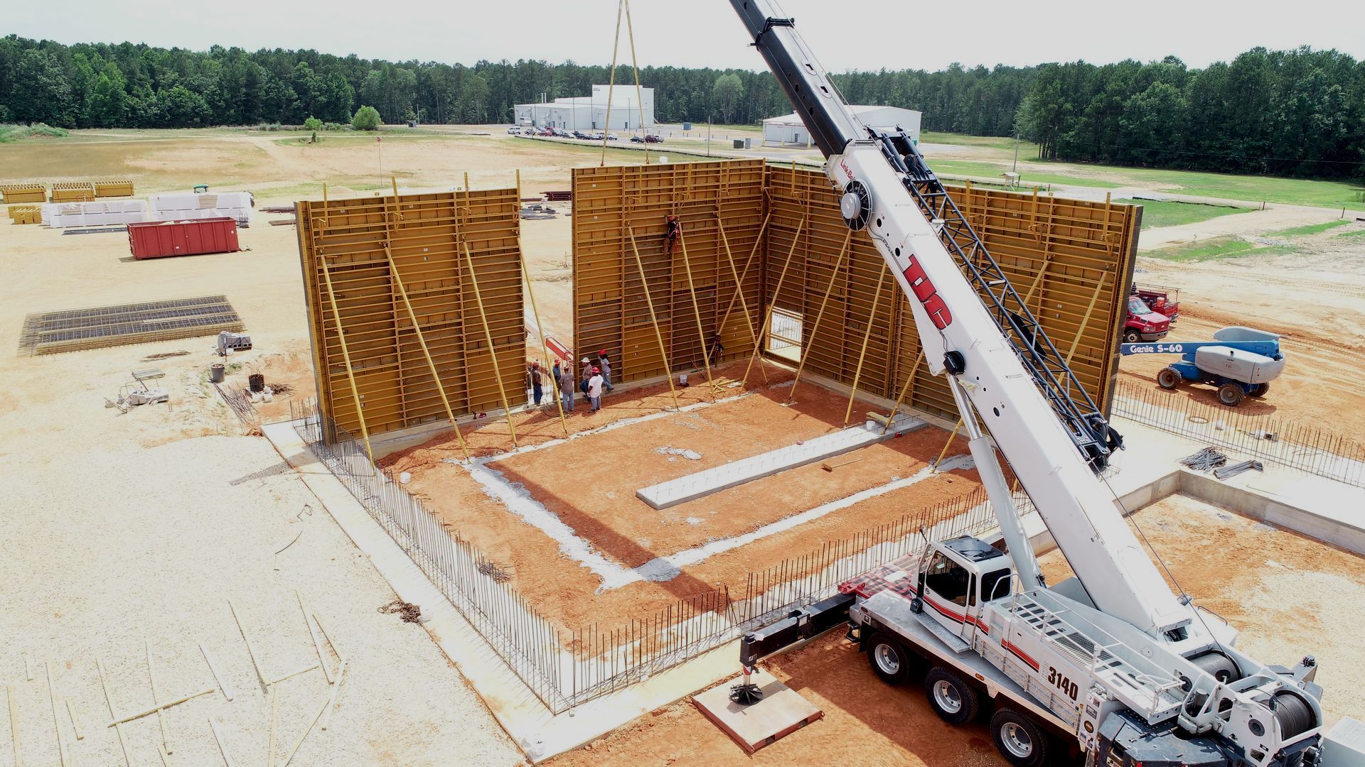 Crane lifting a large wall panel at a construction site with formwork and concrete slab foundation
