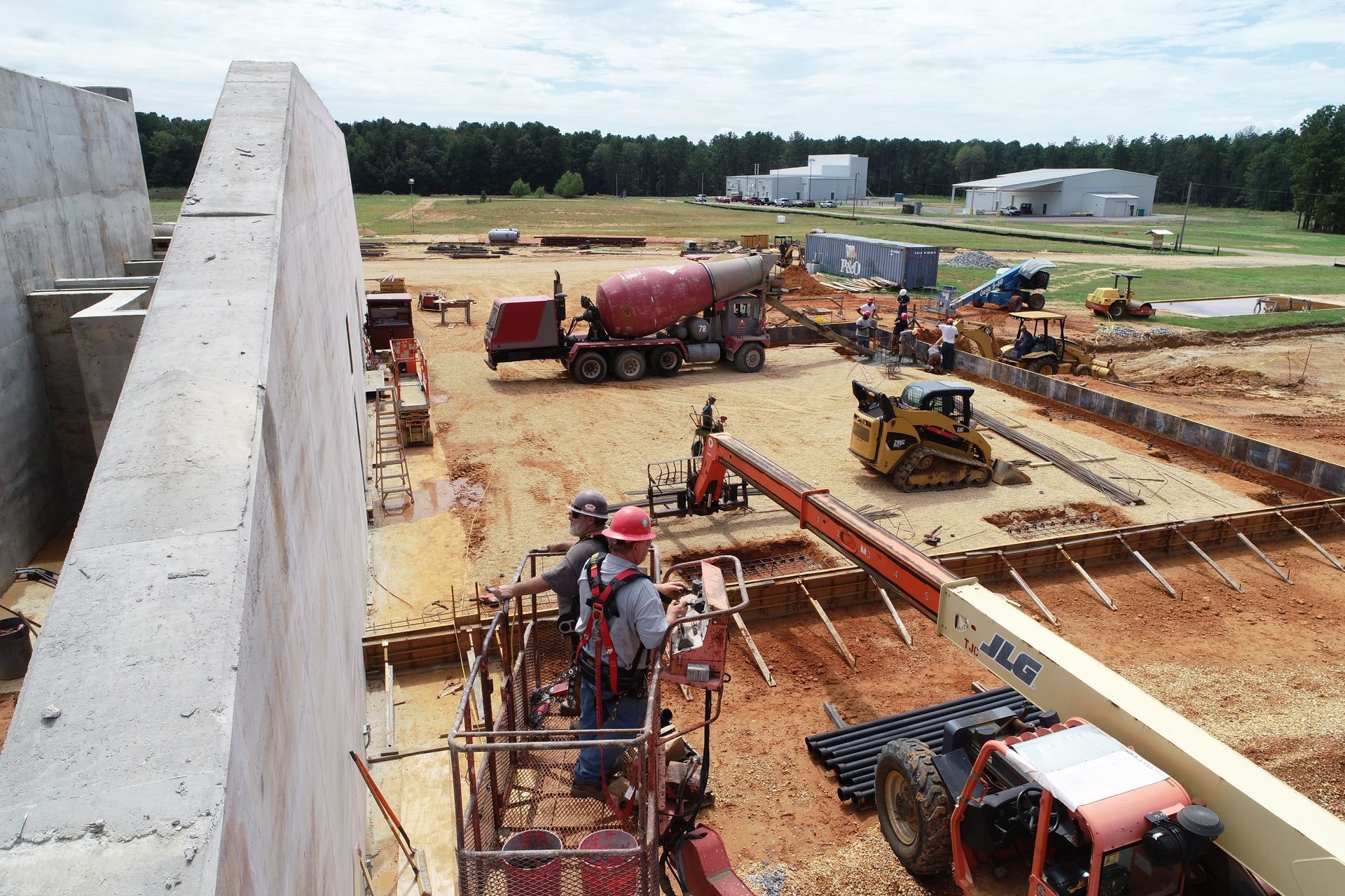 Construction site with workers, concrete forms, and heavy equipment on a dirt foundation