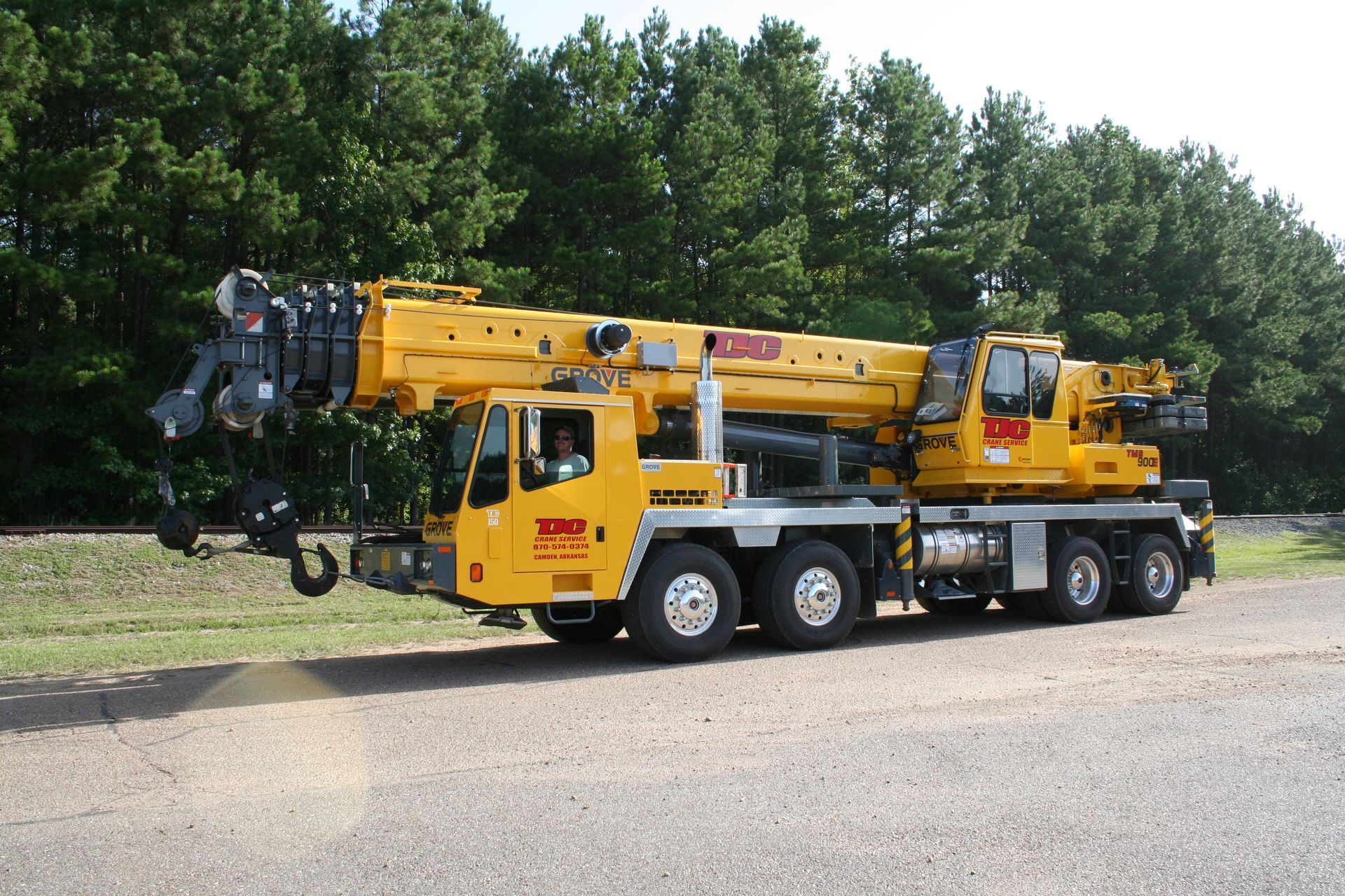 Yellow heavy crane truck parked on a road beside trees