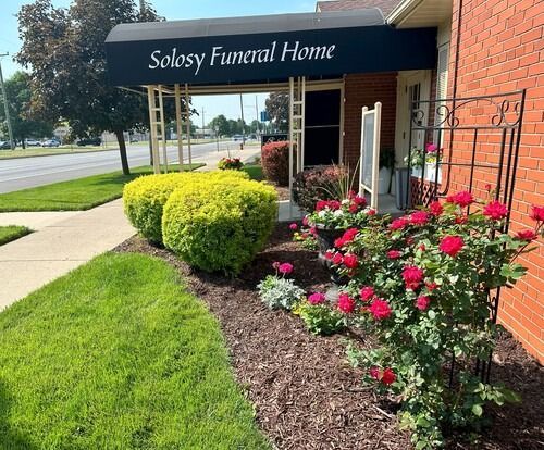 Funeral home entrance with awning, landscaping, and roses. 