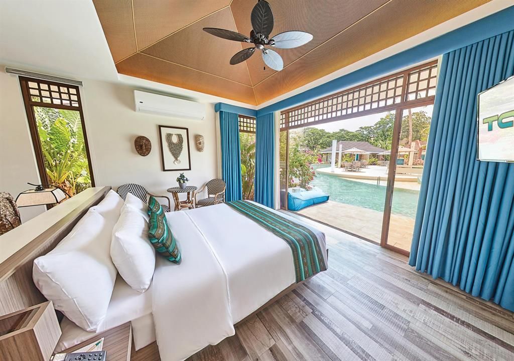 Tropical resort pool with turquoise water, lounge chairs, and thatched-roof villas amid lush greenery