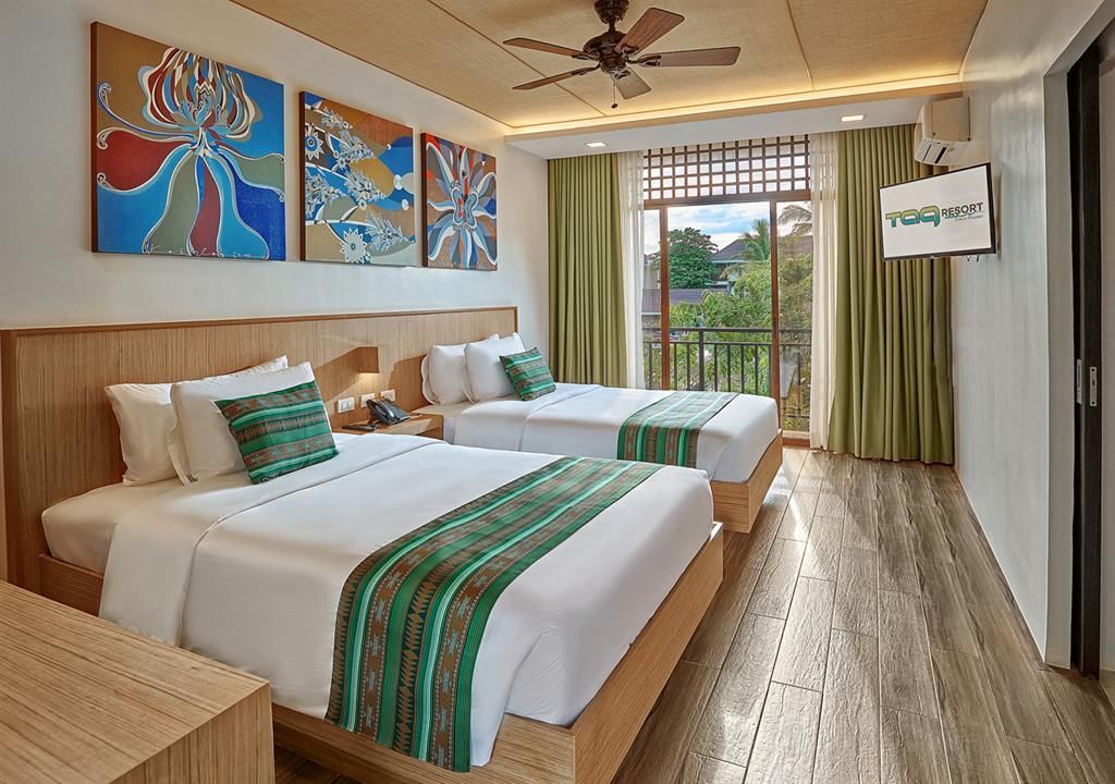 Modern hotel room with two beds, colorful wall art, and a balcony view of greenery