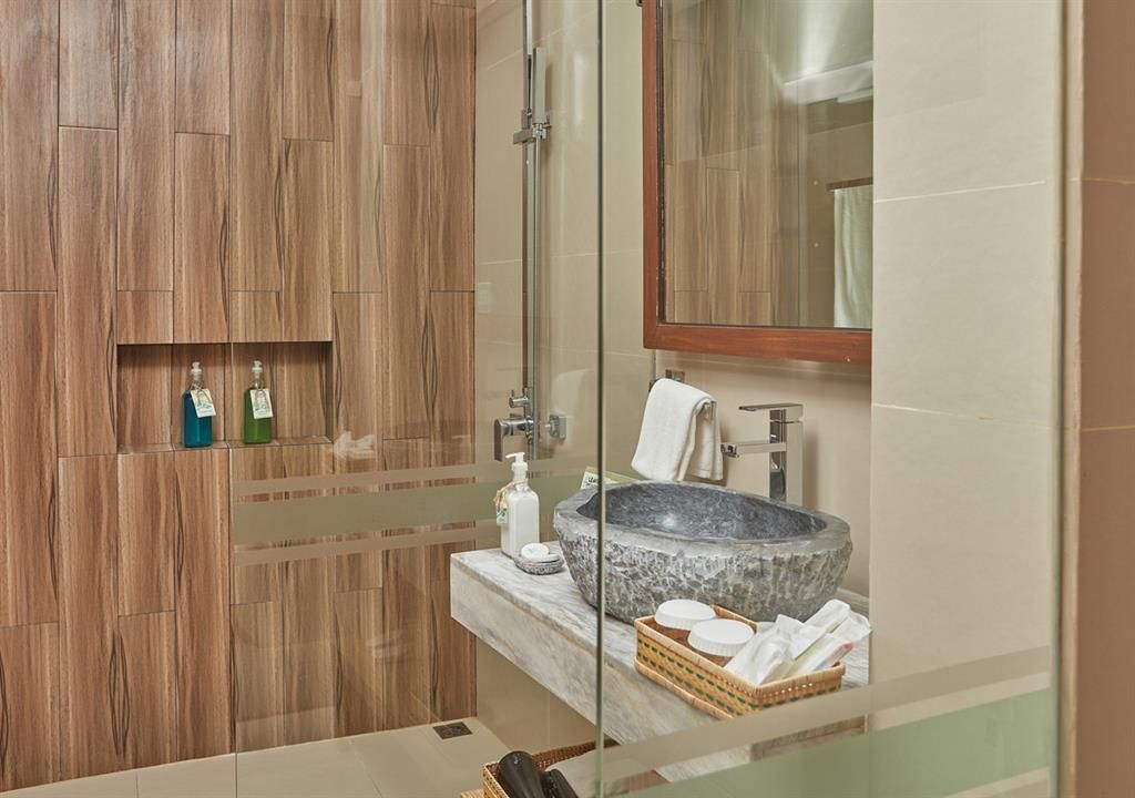 Modern bathroom with wood walls, glass shower, sink, mirror, and toiletries on a woven tray