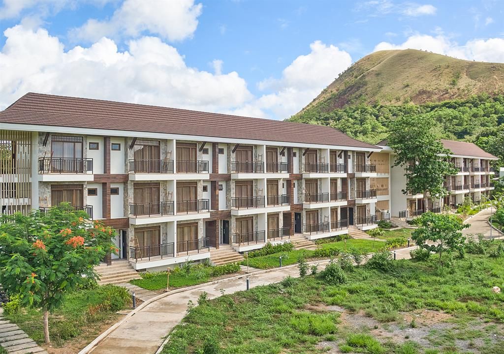 Modern hillside resort with balconies, landscaped gardens, and cloudy sky