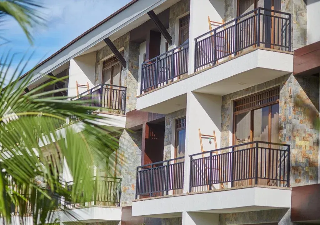 Balconies on a white stucco apartment building with brown railings and tropical palm leaves in front