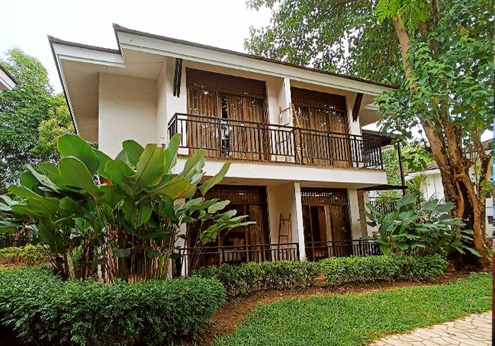 Two-story house with balconies and lush tropical landscaping beside a stone path
