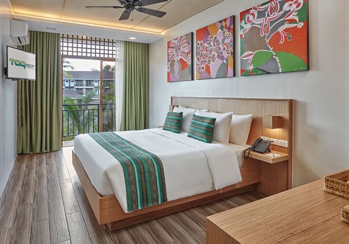Bright hotel room with a king bed, green accents, wall art, and a balcony view.