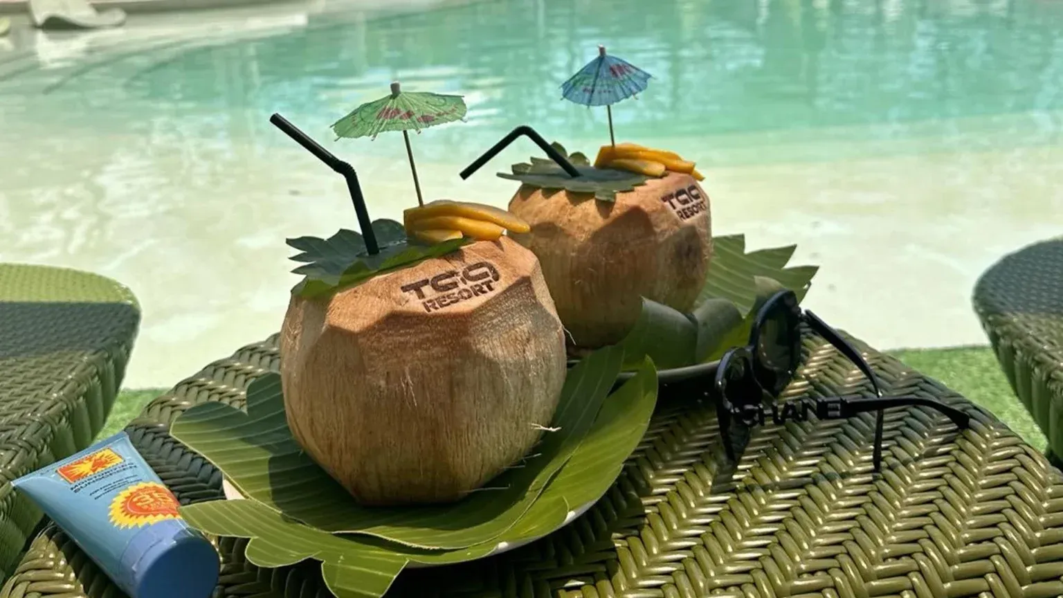 Two coconuts with straws and umbrellas on a leaf placemat beside a black cockroach-like insect.