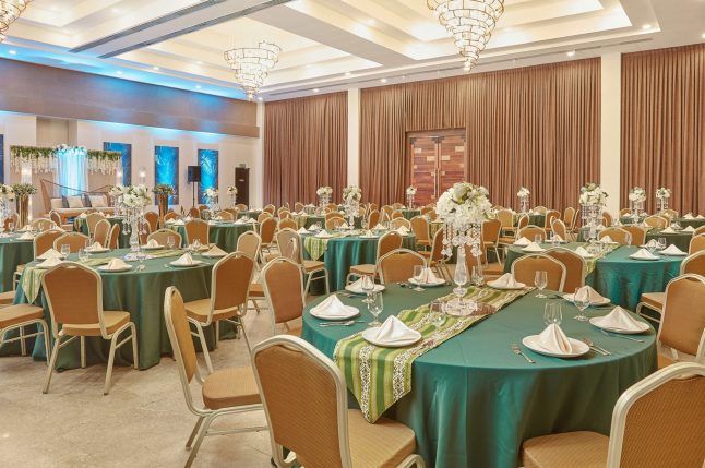 Elegant banquet hall with round, teal tablecloth tables set for a formal event under chandeliers.