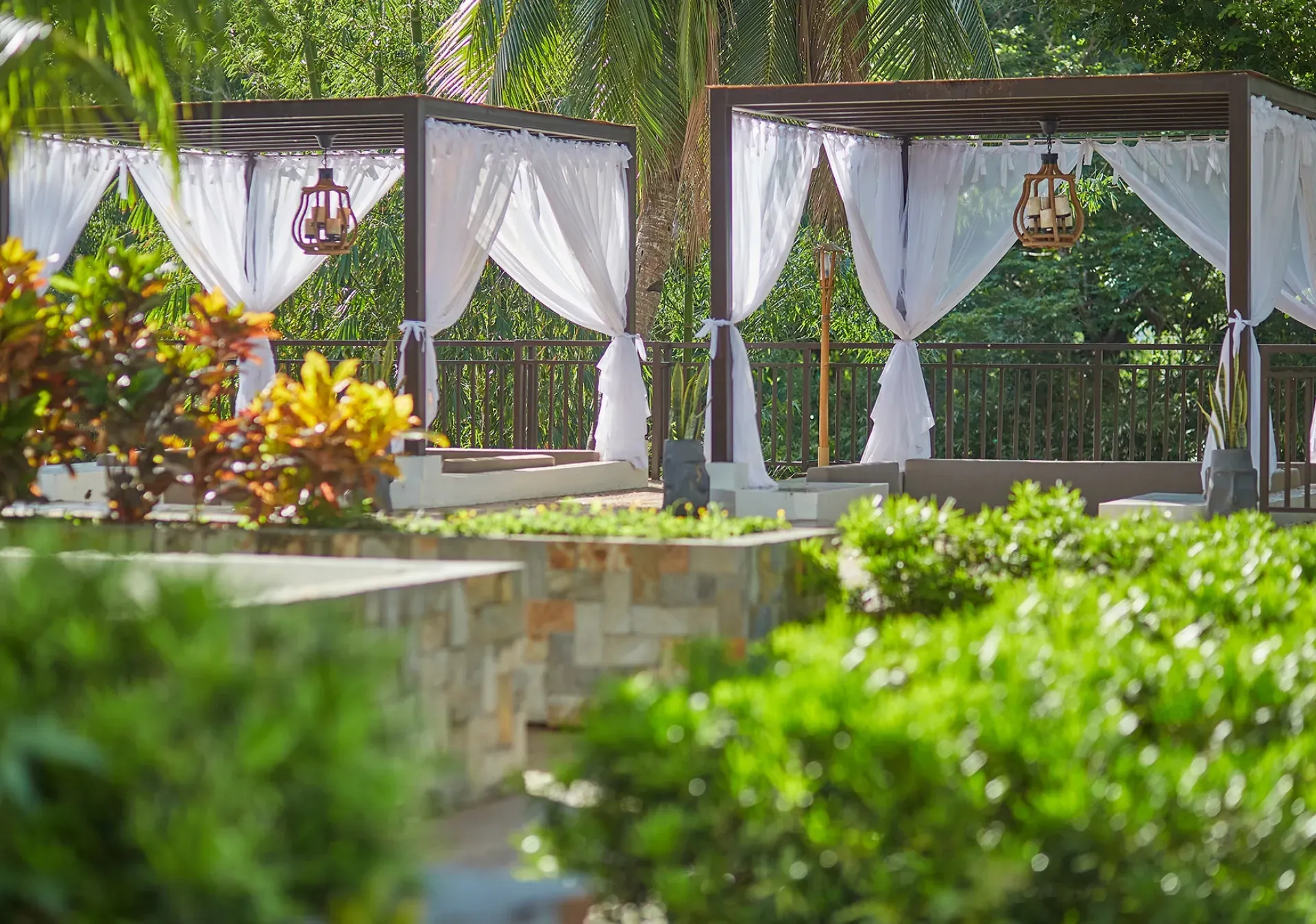 White-draped outdoor gazebo in a lush garden with flowers and greenery