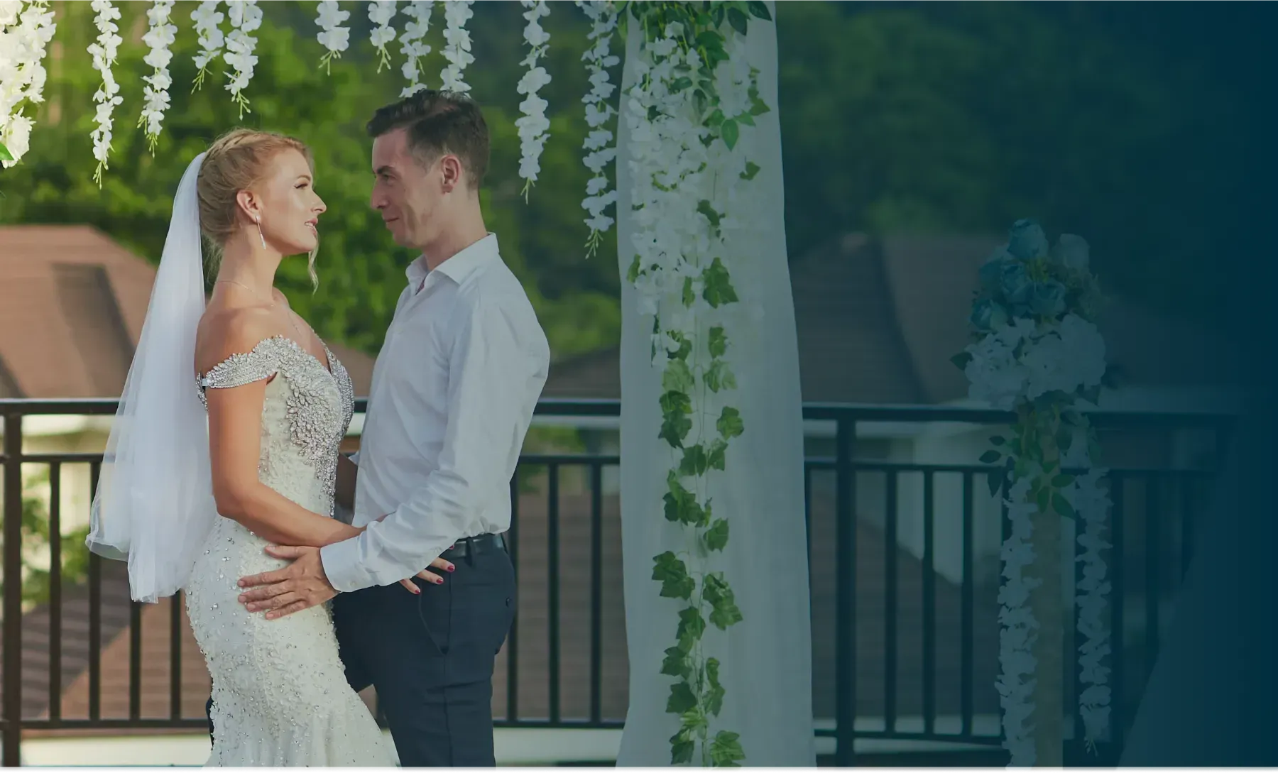 Bride and groom holding hands at a wedding arch with hanging white flowers and greenery