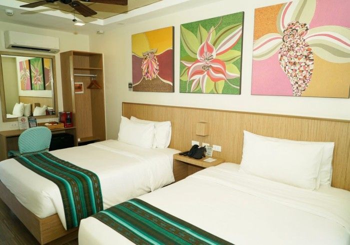 Hotel room with two twin beds, tropical wall art, and warm wood furnishings
