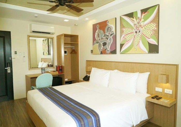 Hotel room with large bed, floral wall art, desk, mirror, and ceiling fan; bright, modern decor