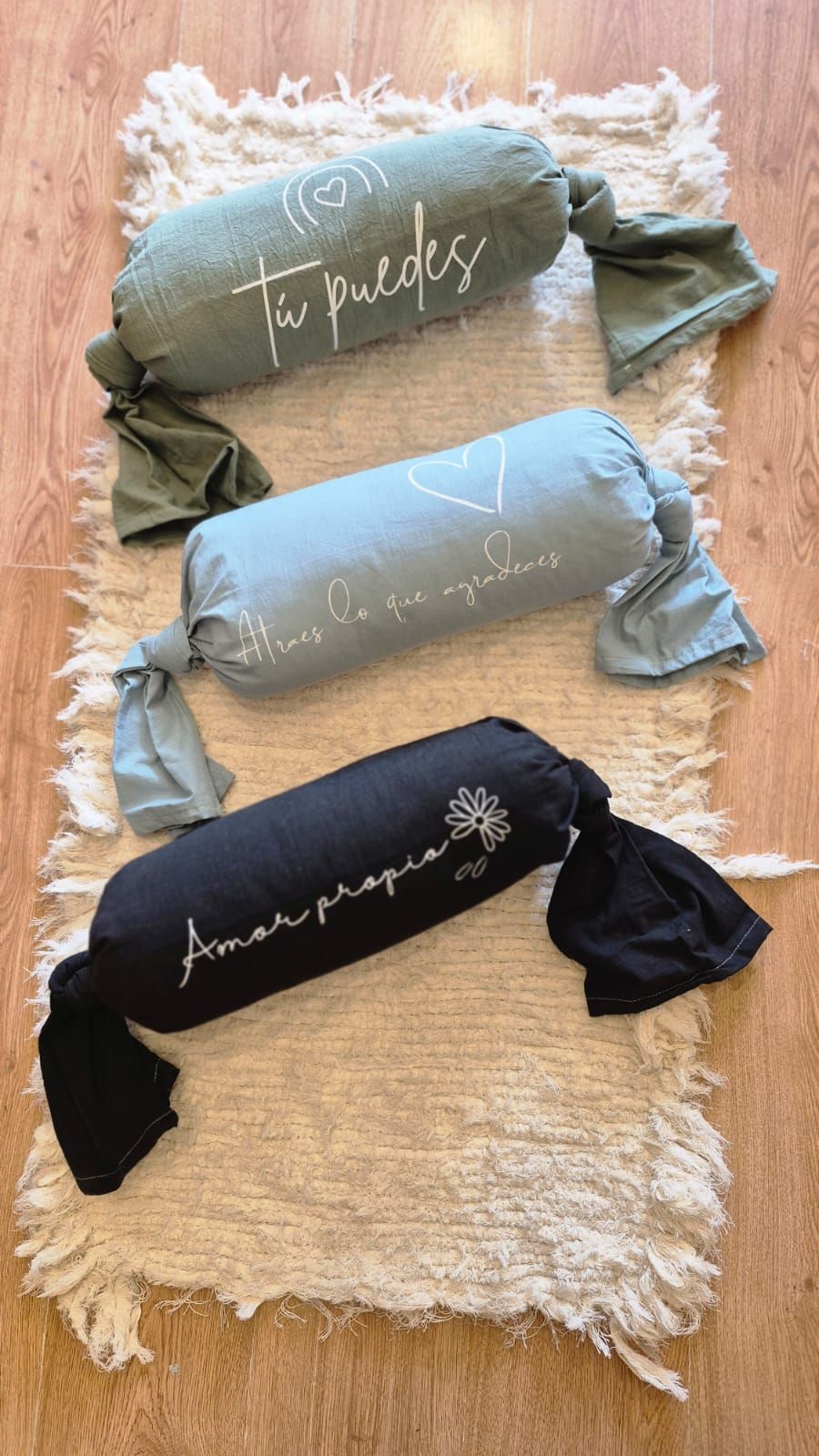 Tres pequeños cojines decorativos bordados sobre una alfombra blanca de pelo largo, en tonos dorados, grises y marrones.