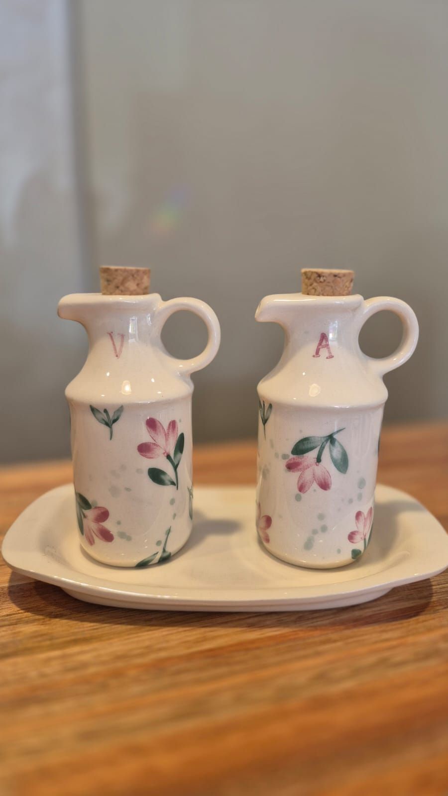 Dos frascos de aceite de cerámica con motivos florales y tapones de corcho sobre un plato blanco en una mesa de madera.