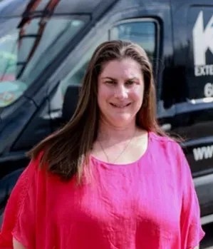 Woman in pink shirt standing in front of a black van with company logo.