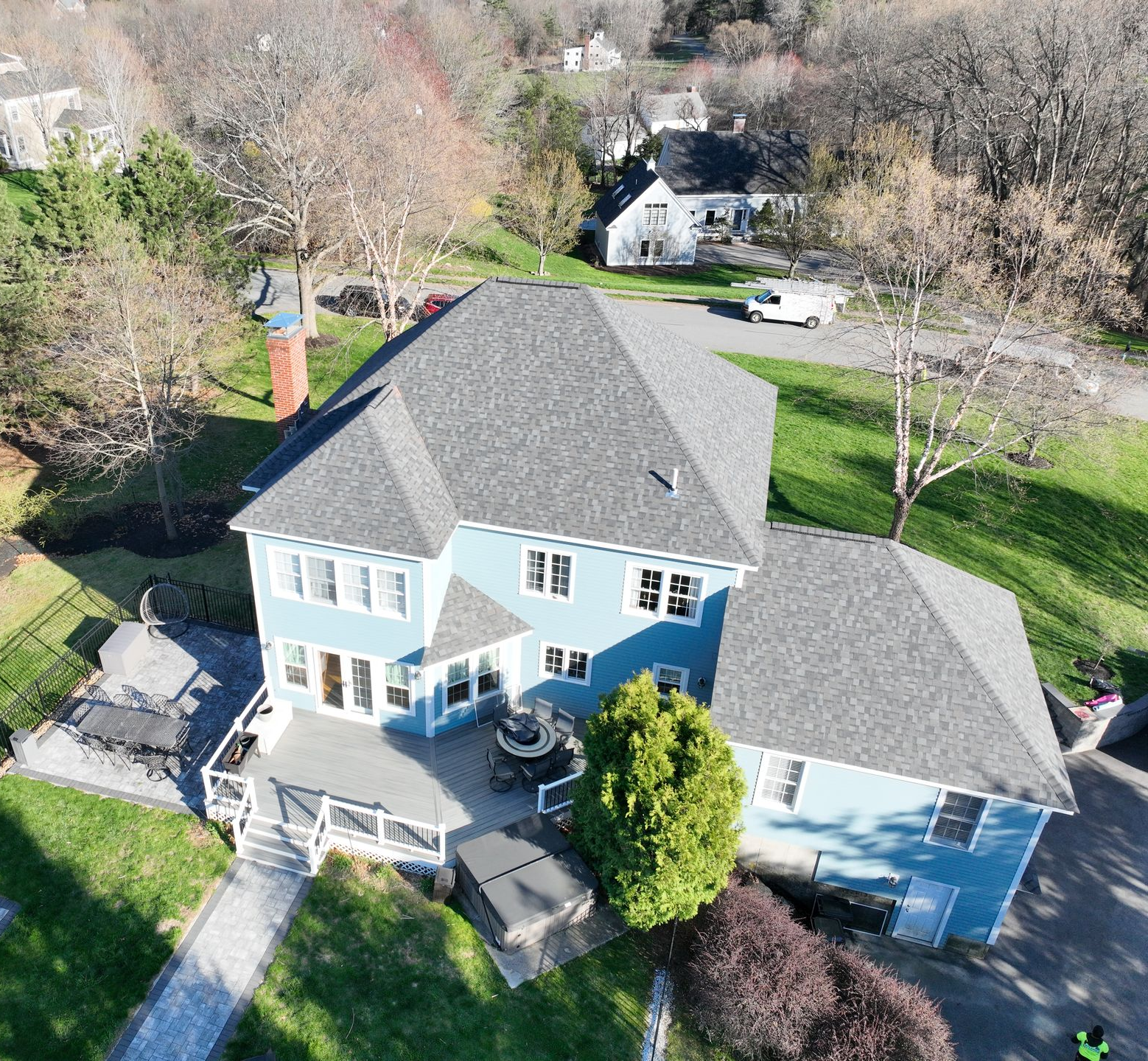 Aerial view of a large blue-gray house with a driveway, trees, and neighboring homes.