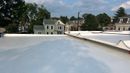 White house with black roof, chimney, and trim, blue sky, and green foliage.