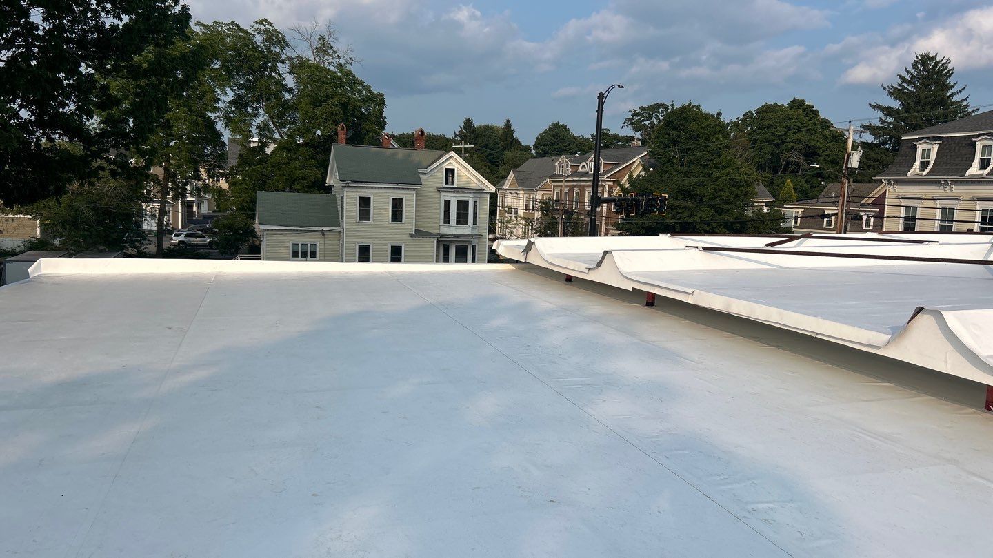 White flat roof with buildings and trees in the background under a partly cloudy sky.