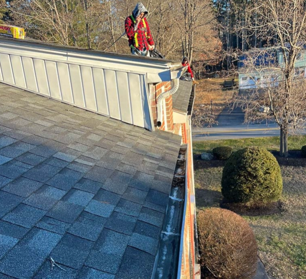 A person on a roof cleans gutters; the scene includes a home and yard with trees.