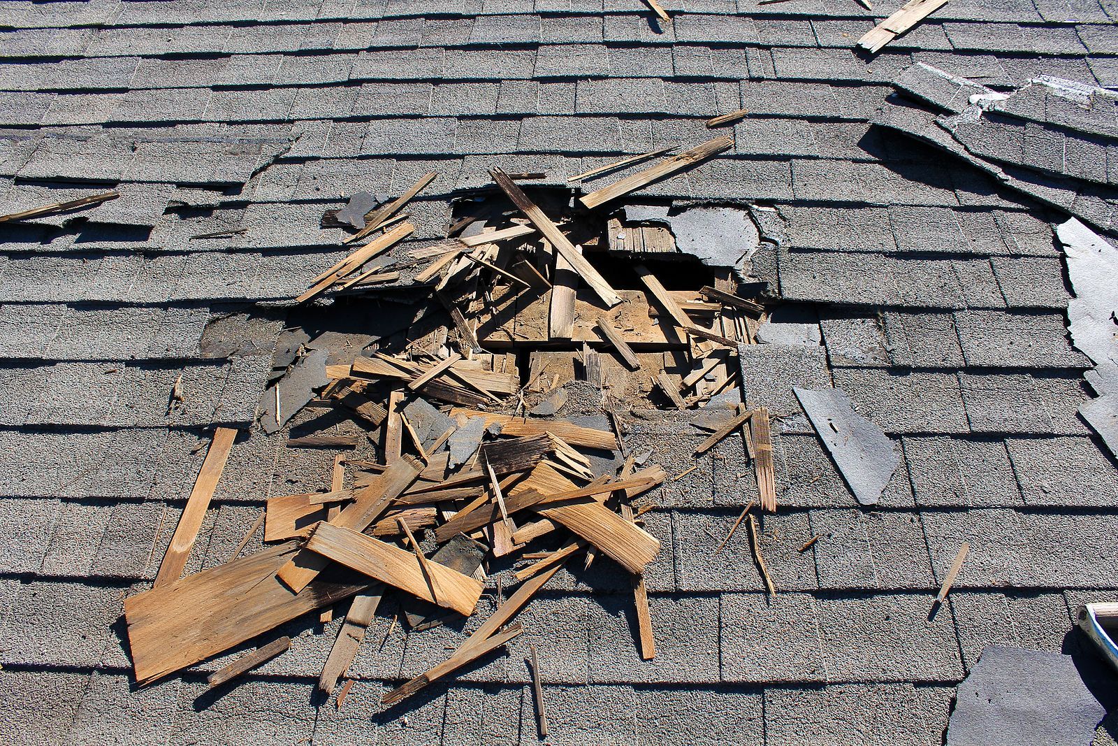 Damaged roof with missing shingles and exposed wood debris.