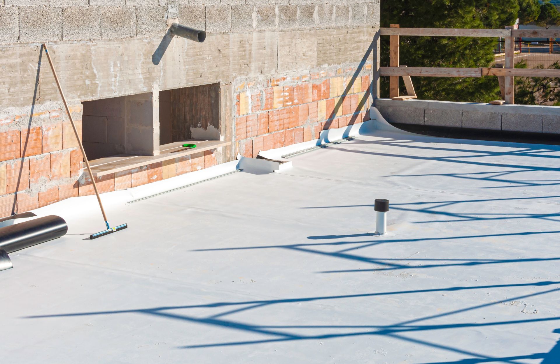 Flat roof construction with white membrane, brick wall, and drainage pipes.