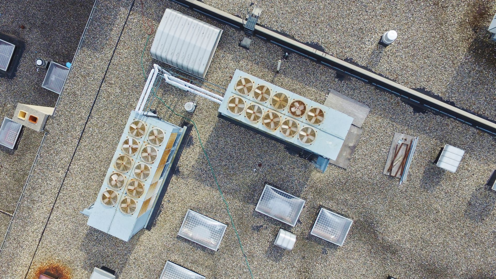 Overhead view of a rooftop with HVAC units, vents, and other equipment against a mottled brown surface.