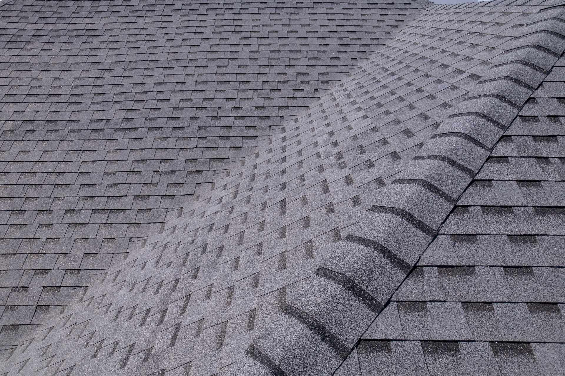 Gray asphalt shingle roof, angled view of two roof sections meeting at a ridge.