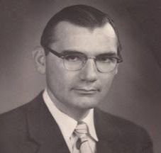 Man in glasses, suit and tie, looking directly at the viewer, studio portrait.