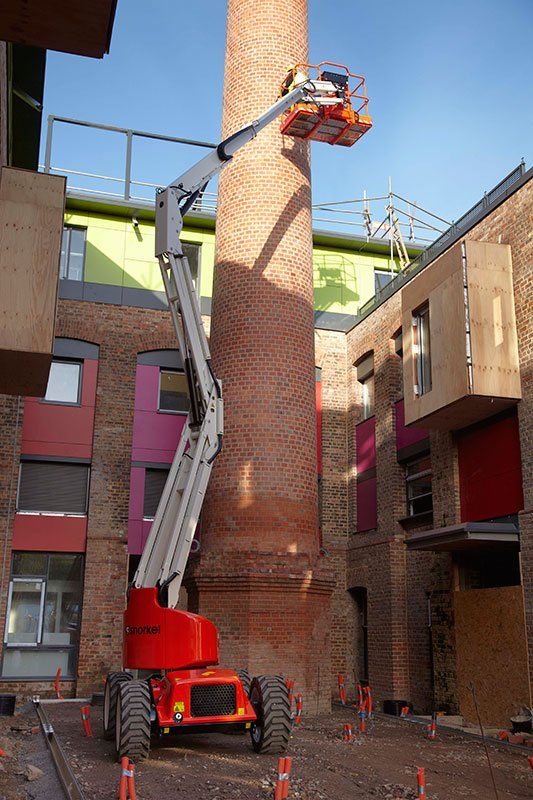 Un hombre está trabajando en una chimenea de ladrillo con una grúa.