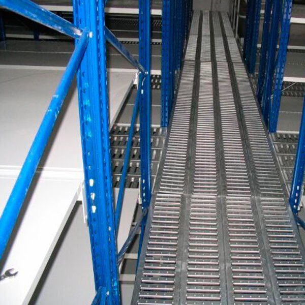 Un almacén con estantes azules y una pasarela metálica.
