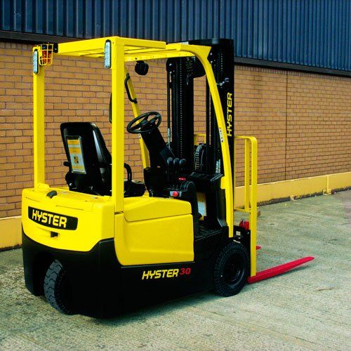 Una carretilla elevadora Hyster amarilla está estacionada frente a un edificio de ladrillo