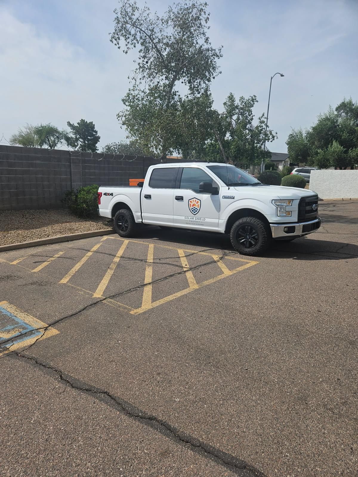 White pickup truck parked in a yellow crosshatched lot beside a brick wall and trees