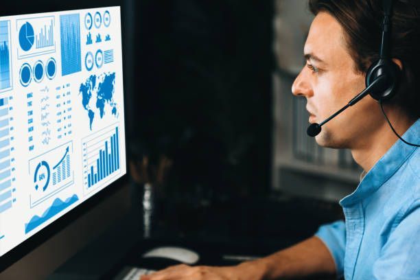 Customer support agent wearing a headset reviews blue analytics dashboards on a computer monitor