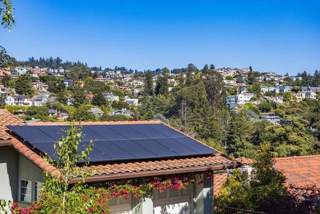 Rooftop solar panels overlooking a leafy hillside neighborhood under a clear blue sky
