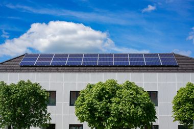 Solar panels on a building roof above green trees under a blue sky