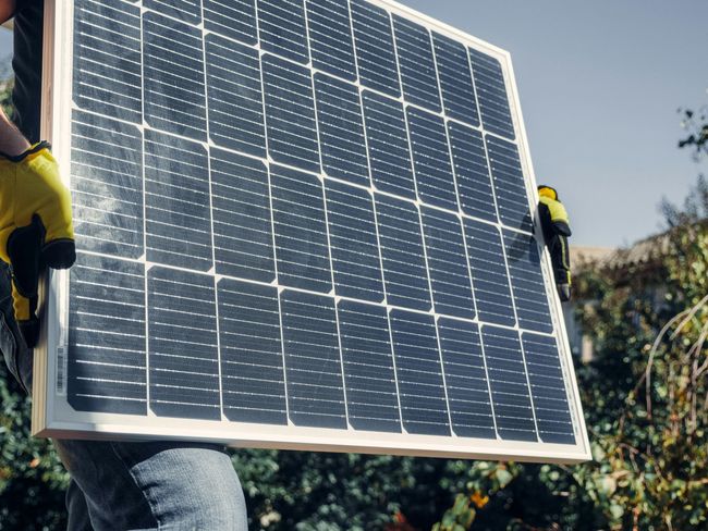 Two workers carrying a large solar panel outdoors on a sunny day