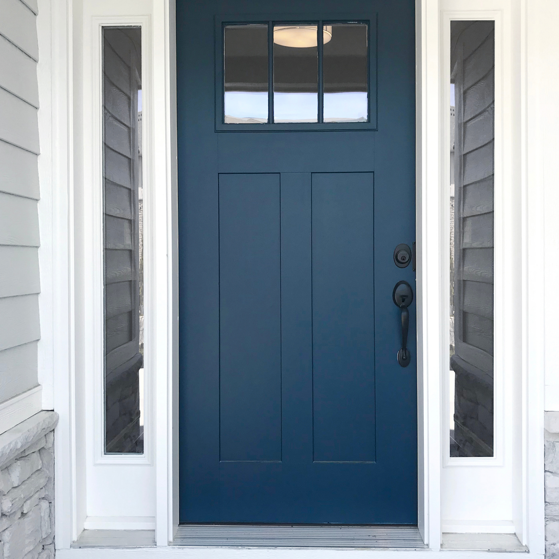 A blue front door with white trim and windows on a white house.