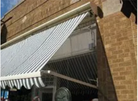 A striped awning is hanging from the side of a brick building.