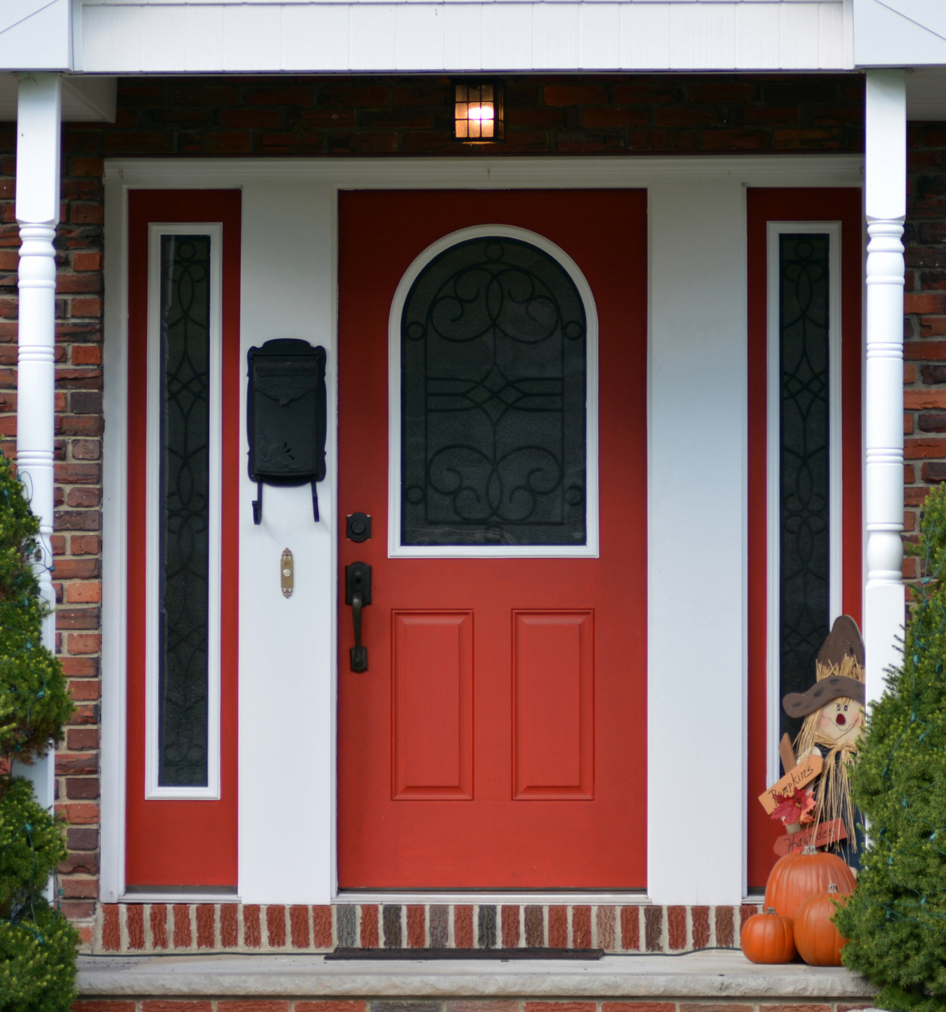 A red door with a scarecrow and pumpkins in front of it