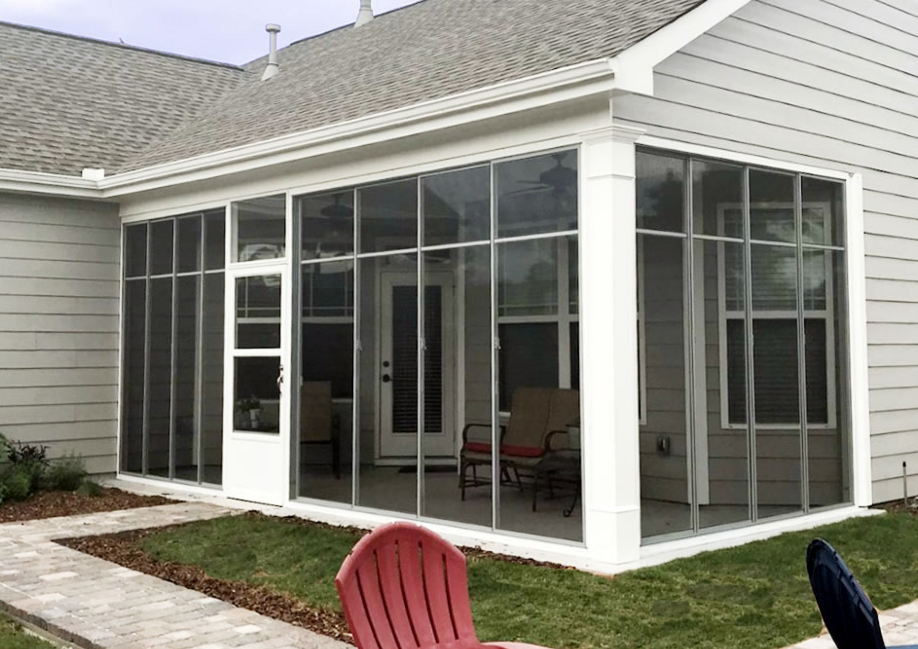 A screened in porch with chairs and tables in front of a house.