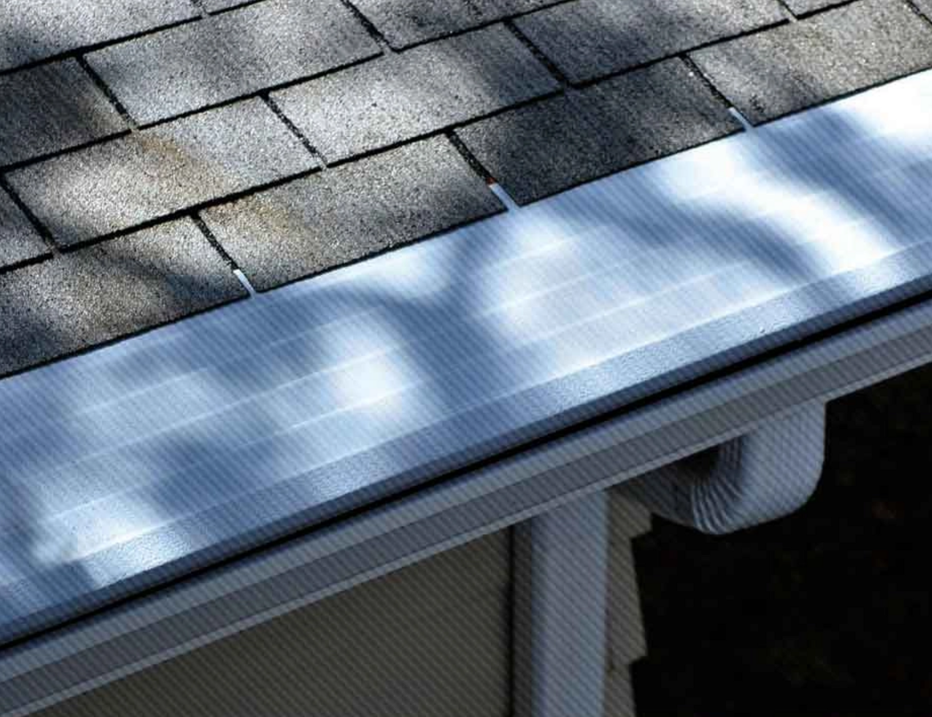 A close up of a gutter on a roof with a tree shadow on it.