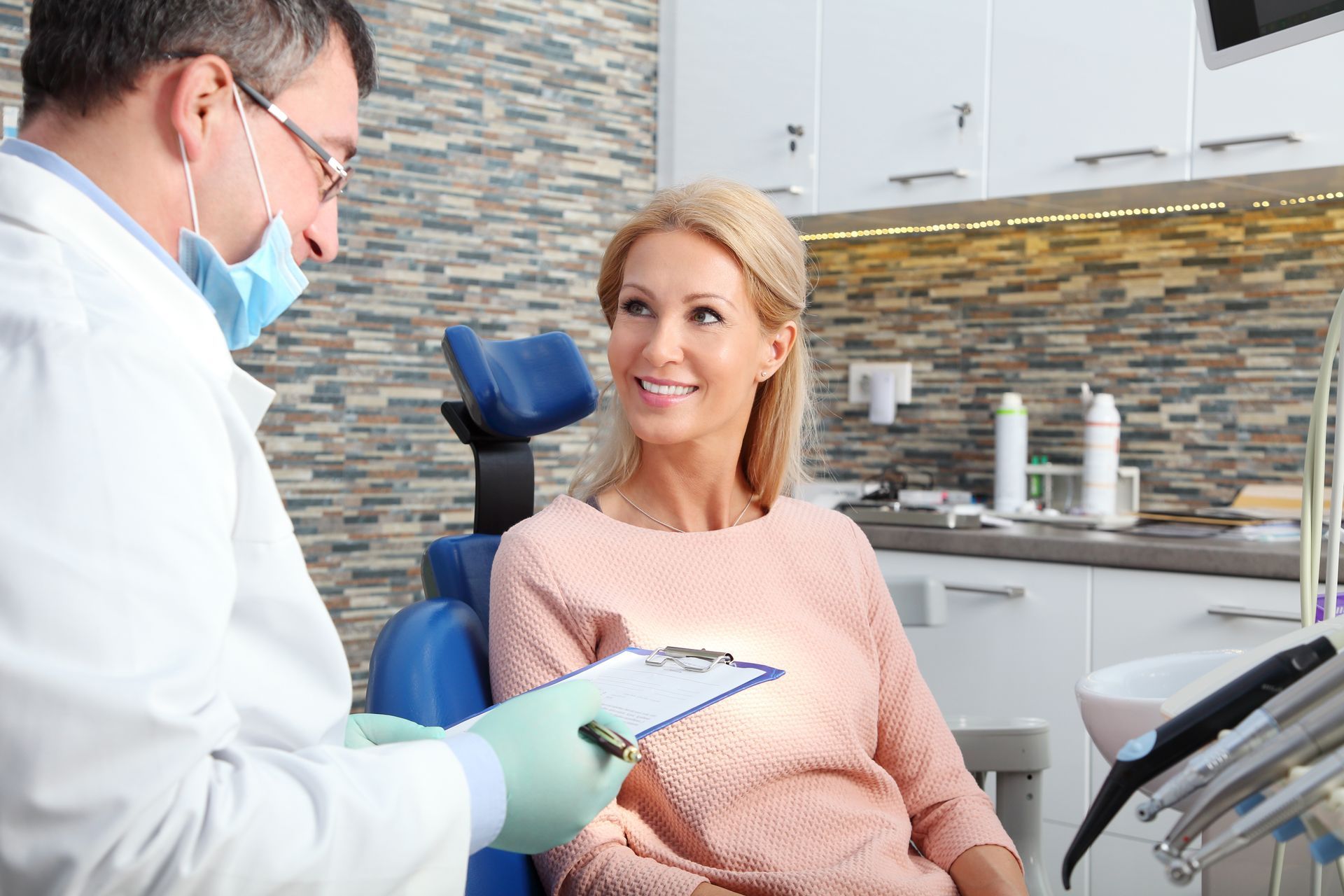 A dentist examining a smiling patient holding a blue tooth-shaped mirror in a clinic