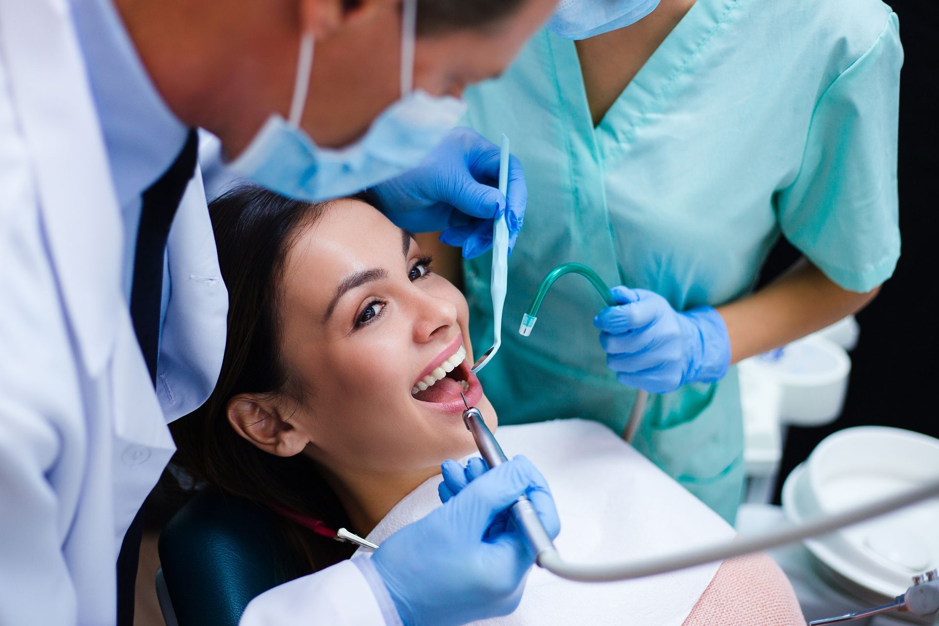 Dentist treating a smiling patient in a dental clinic with tools and a mask worn by staff.