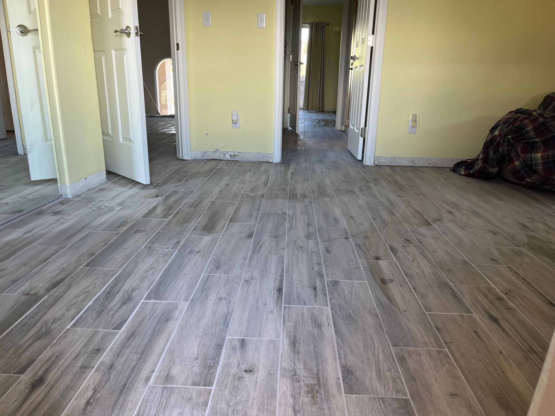 Empty room with gray wood-look flooring, pale yellow walls, open doors, and a plaid blanket on the right.