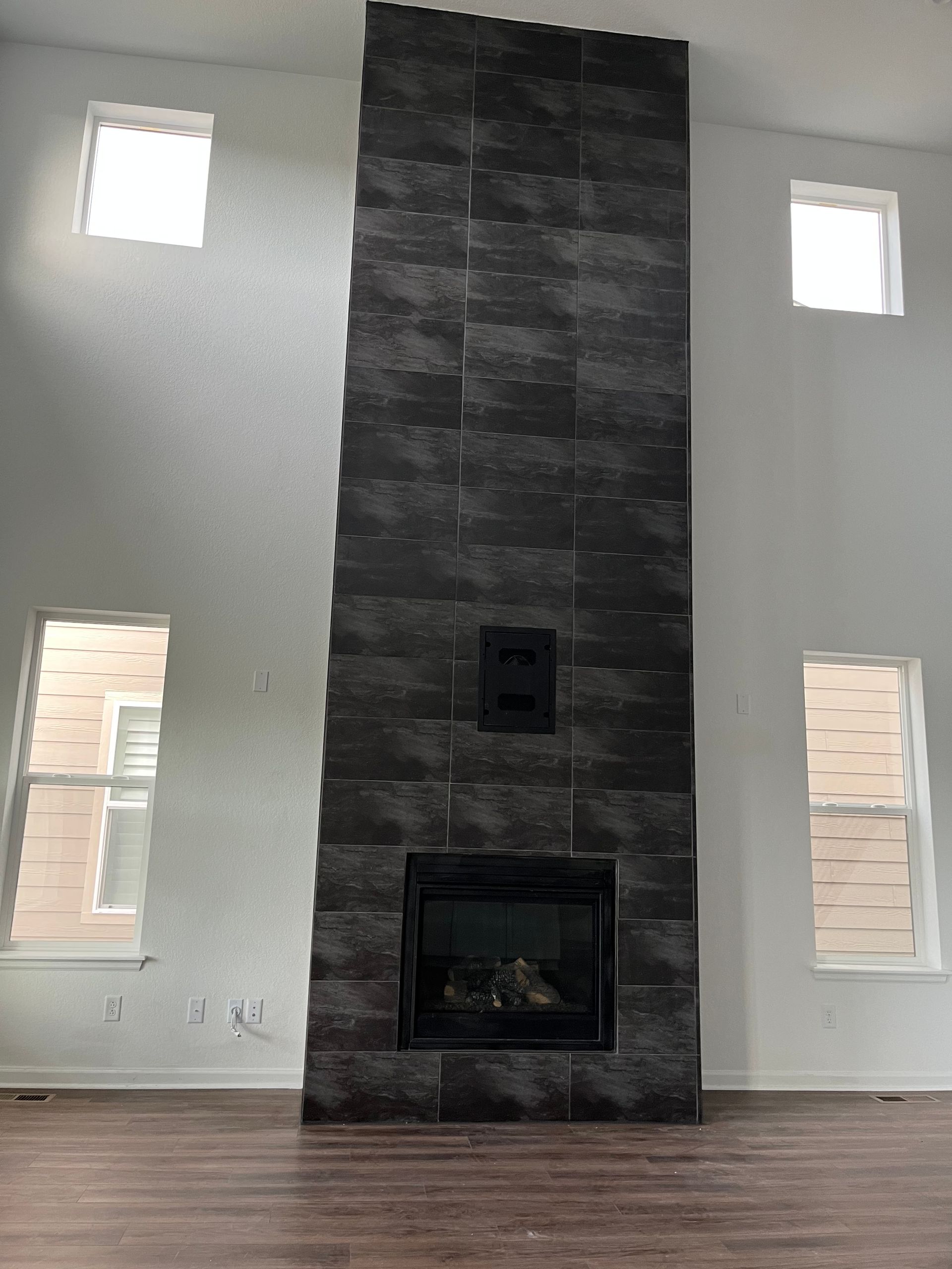 Modern living room with a dark stone fireplace centered between tall narrow windows.