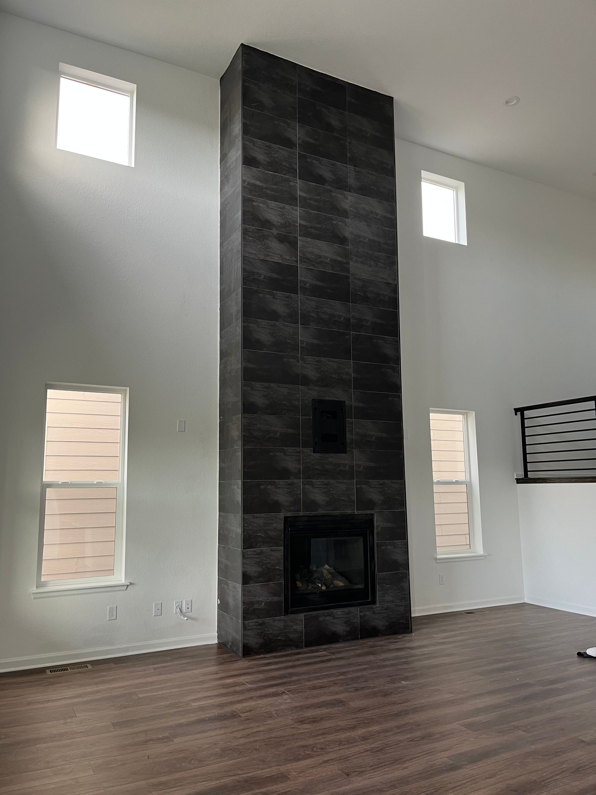Modern empty living room with a tall black stone fireplace and hardwood floor