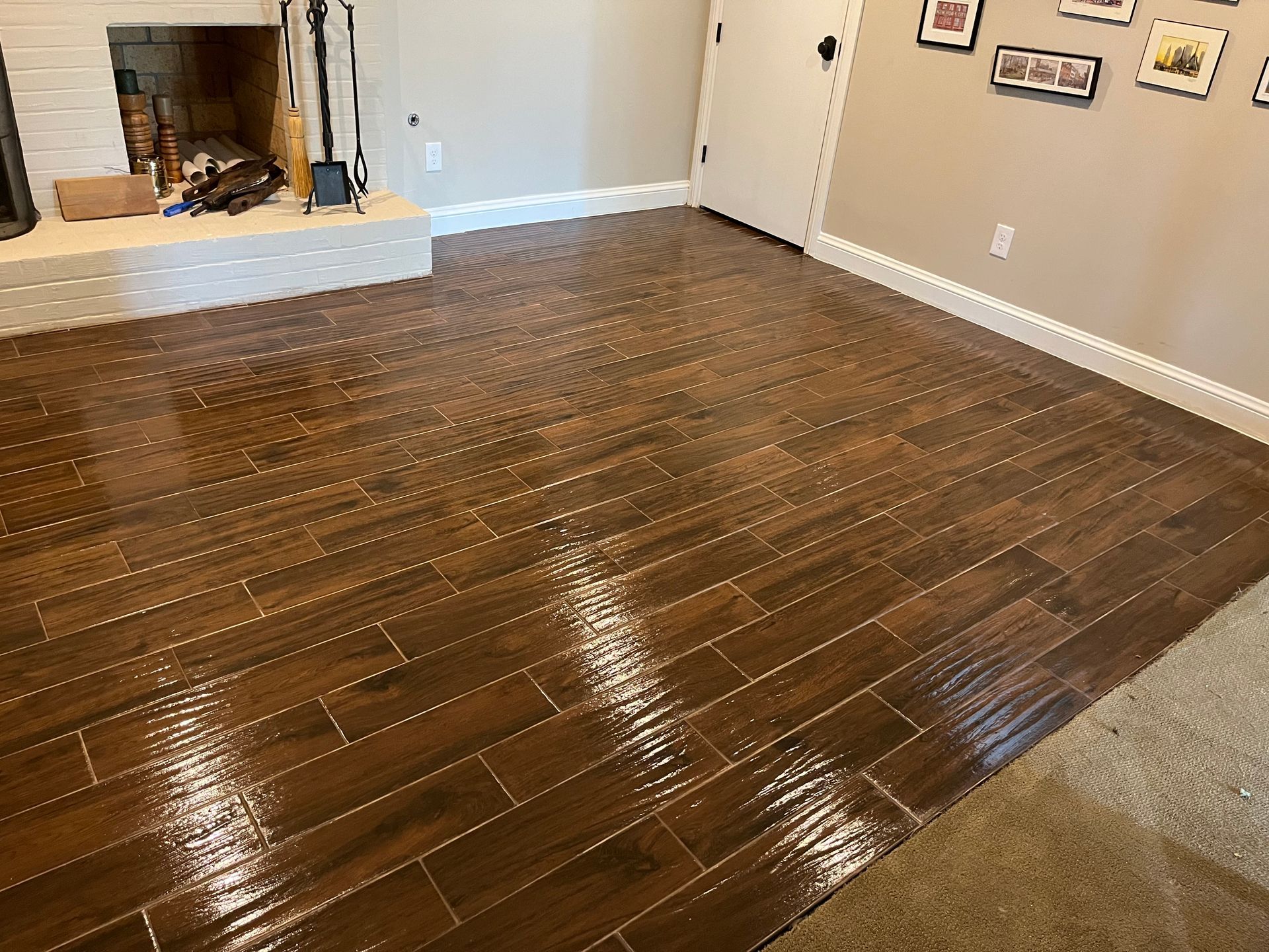 Empty living room with dark glossy wood floors, beige carpet, fireplace, and wall art